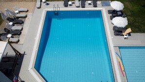 Une piscine rectangulaire, bordée d’une terrasse carrelée, entourée de chaises longues et de parasols.