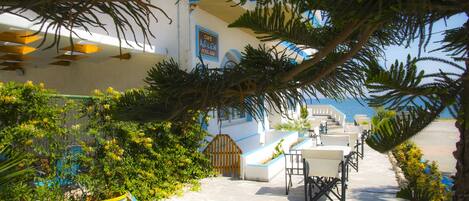 A coastal building with a pool area, outdoor seating, and a view of the sea.