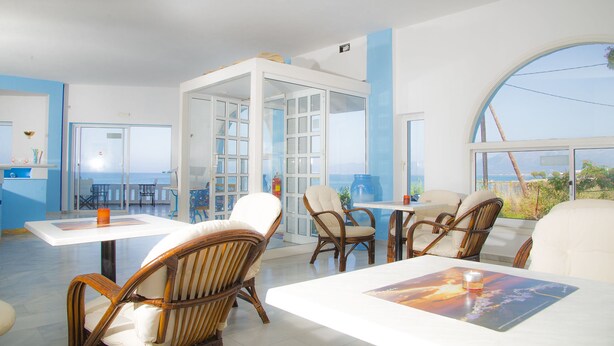 Une pièce spacieuse avec une grande fenêtre donnant sur la mer. On y trouve plusieurs fauteuils en osier et une table sur laquelle sont posés une bougie et un magazine.