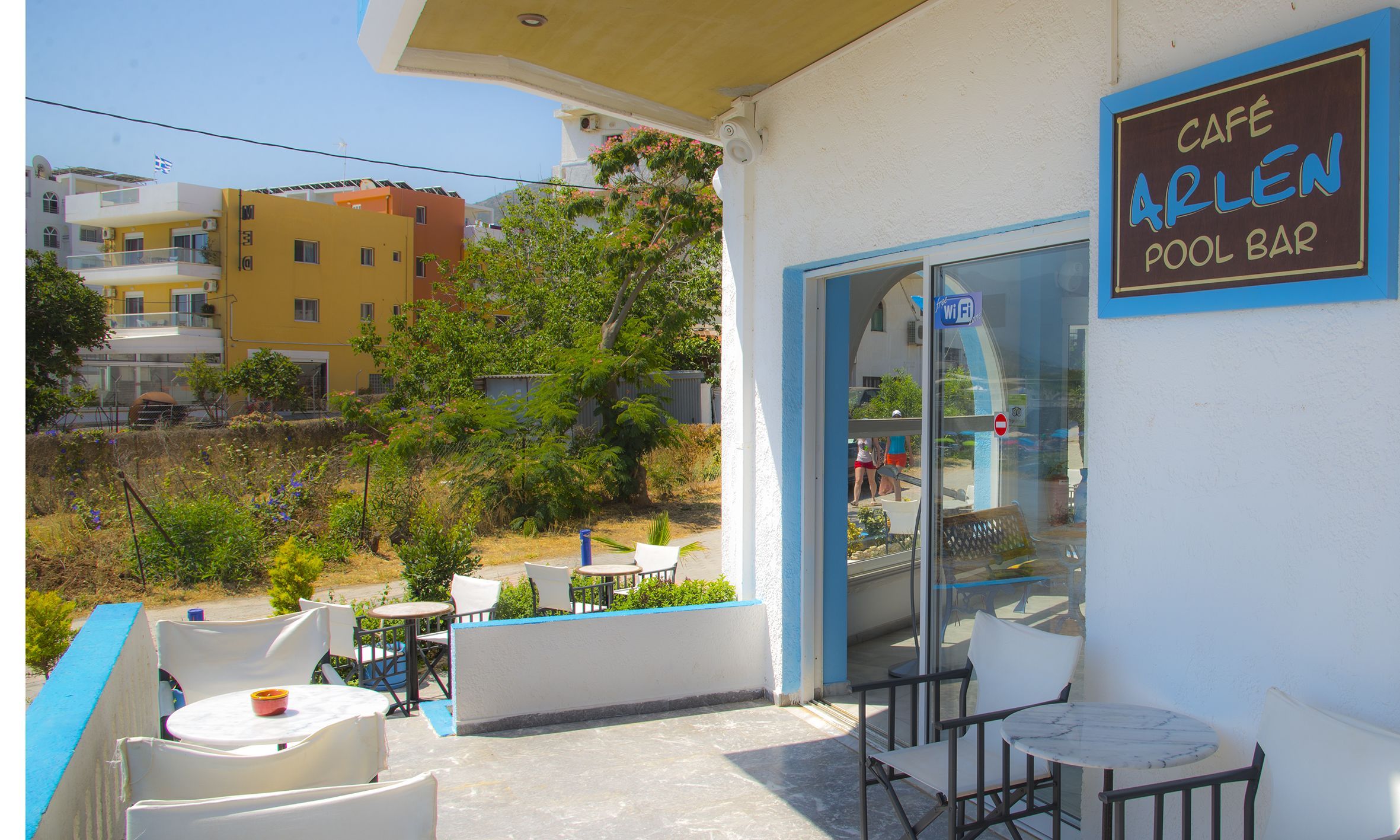 A café with outdoor seating, a pool bar sign, and a view of the surrounding buildings.