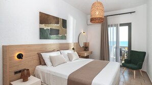 Une chambre d’hôtel moderne avec un grand lit, une table de chevet avec une lampe, un fauteuil vert, un balcon avec vue et une œuvre d’art accrochée au mur.