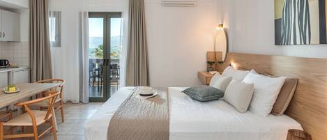 A hotel room with a bed, a desk with chairs, a dining table, a balcony with curtains, and a painting on the wall.