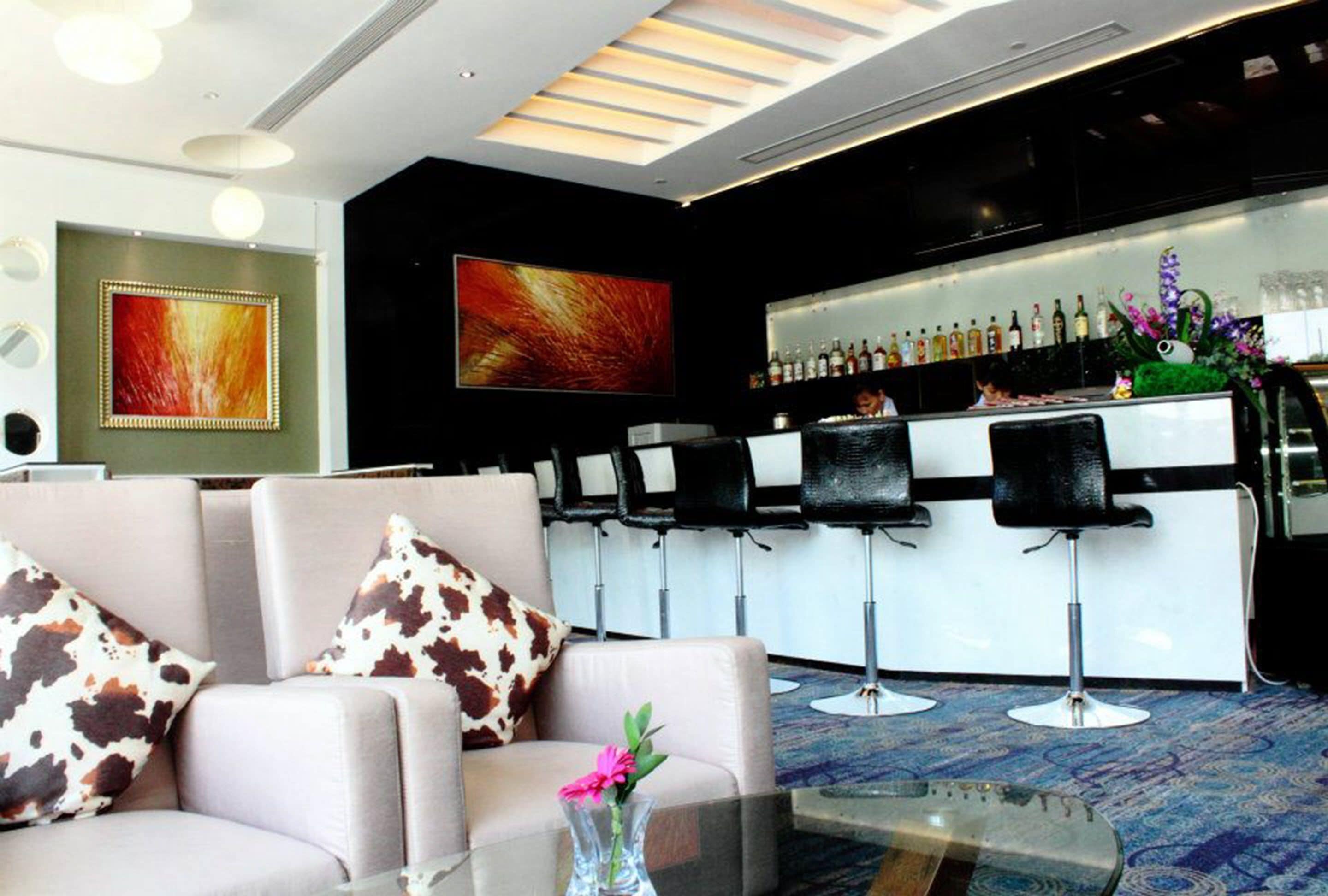 A modern bar area with a sofa and chairs, a bar counter with bottles, and a large abstract painting on the wall.