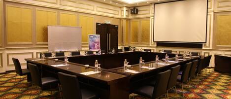 A conference room with a long table, chairs, a whiteboard, a projector screen, and a carpeted floor.