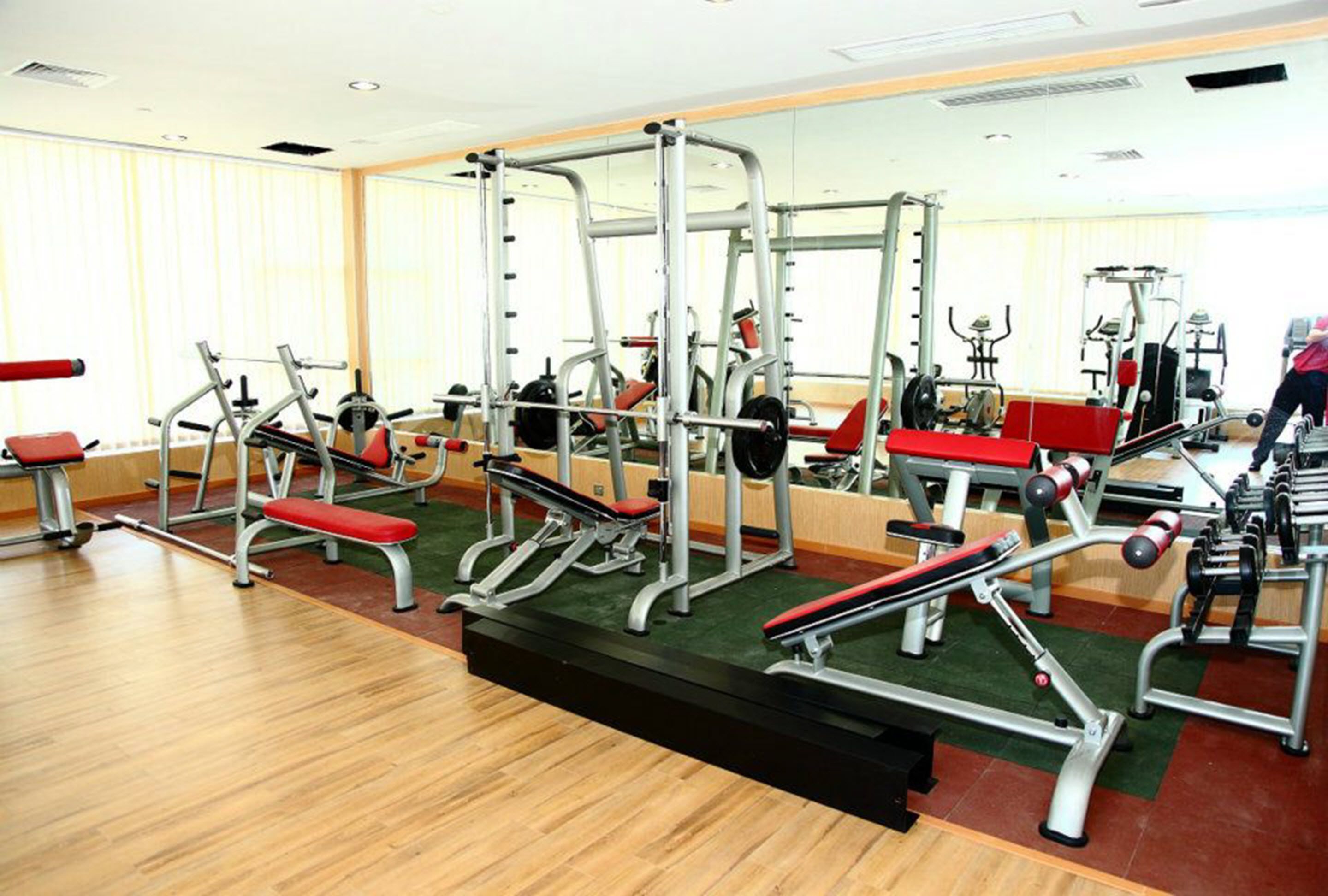 A gym with various exercise machines, a mirror, and a wooden floor.