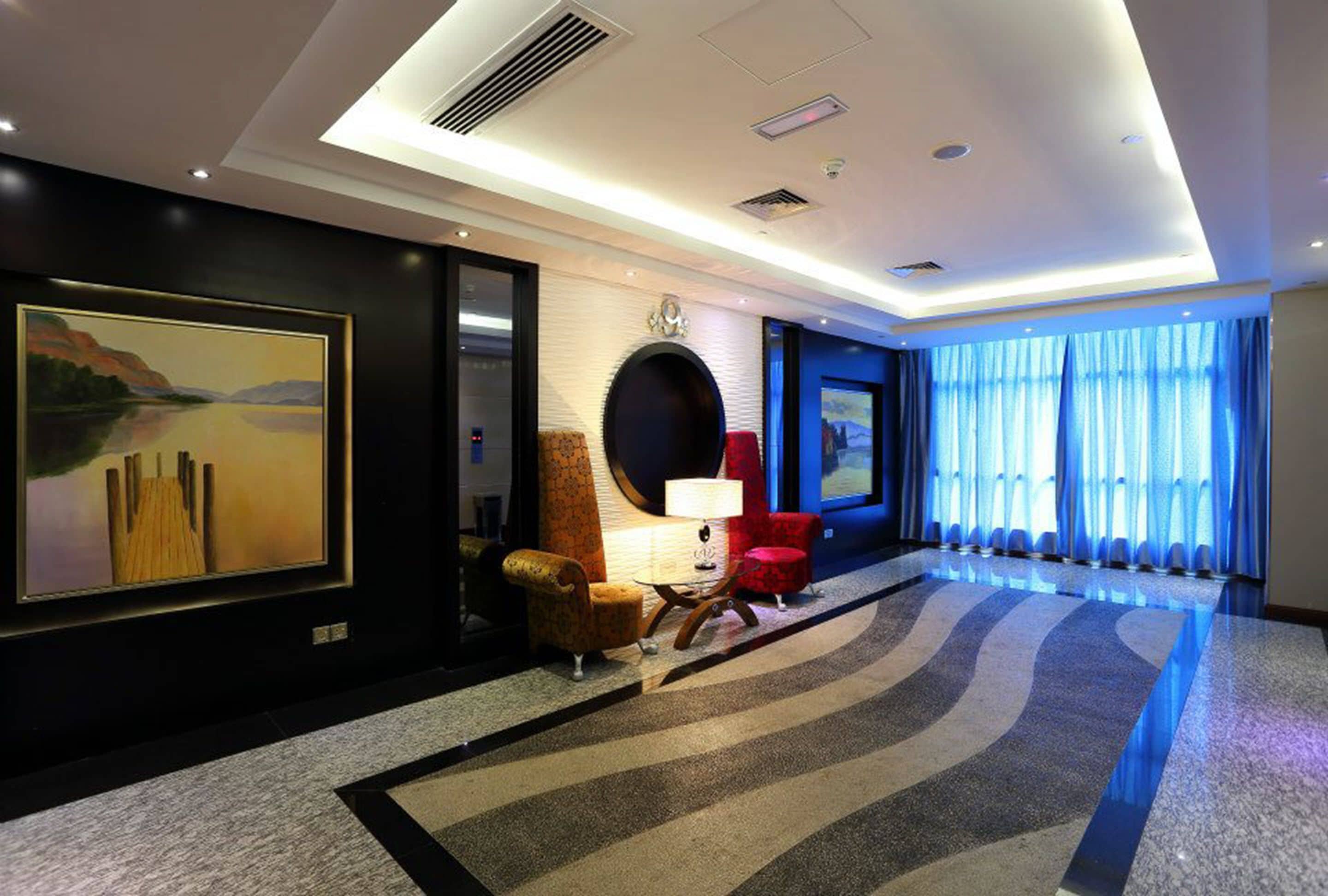 A modern hotel lobby with a large painting, a round table with a lamp, and a red chair.