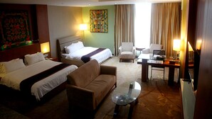 A hotel room with two beds, a sofa, a glass coffee table, and a desk with a lamp.