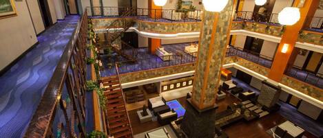 A multi-level hotel lobby with a central staircase, seating areas, and a pool.