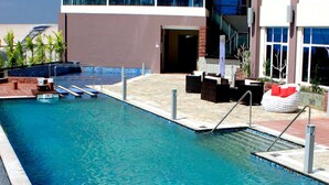 A swimming pool with a sun deck, lounge chairs, and a building with large windows and a staircase. - Meritz Hotel (Miri)