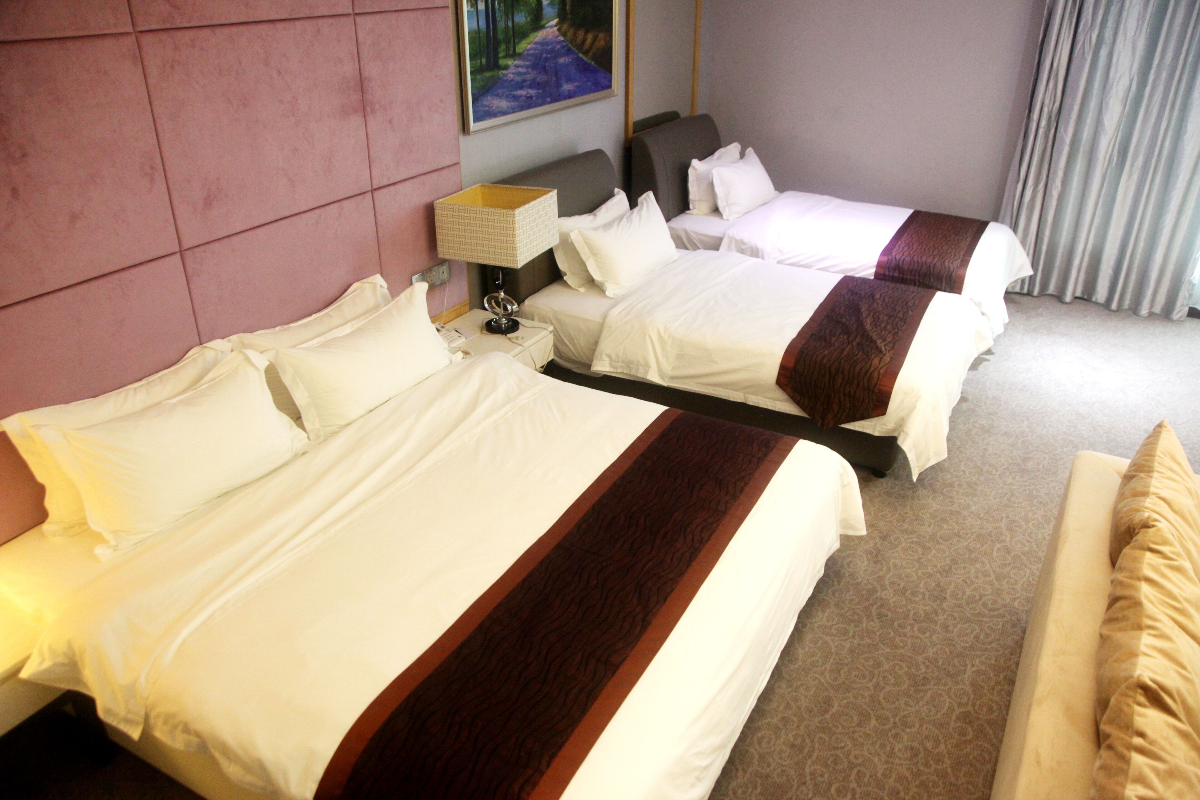 A hotel room with two beds, a nightstand, a lamp, and a painting on the wall.