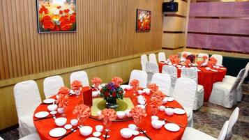 A banquet hall with round tables covered in red tablecloths, white chairs, and floral centerpieces.