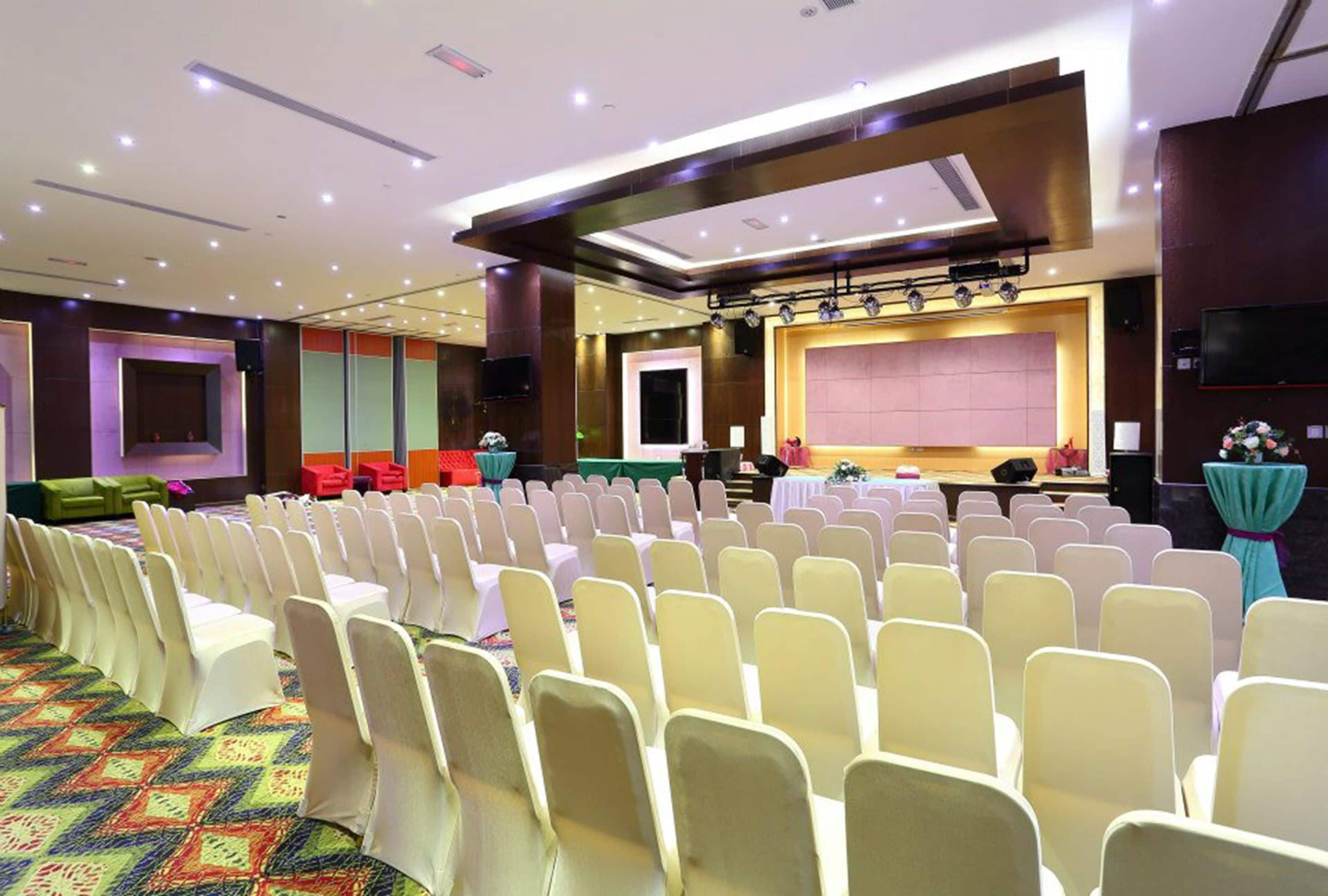A conference room with rows of chairs, a stage, and a large screen.