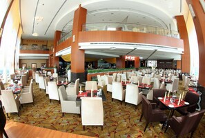 A spacious hotel lobby with multiple dining areas, a central atrium, and a second-floor balcony.
