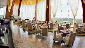 A spacious restaurant with high ceilings, large windows with yellow curtains, and a view of the outdoors. - Meritz Hotel (Miri)