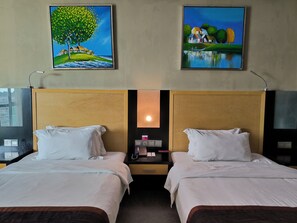 A hotel room with two beds, a nightstand with a phone and a lamp, and two paintings on the wall.