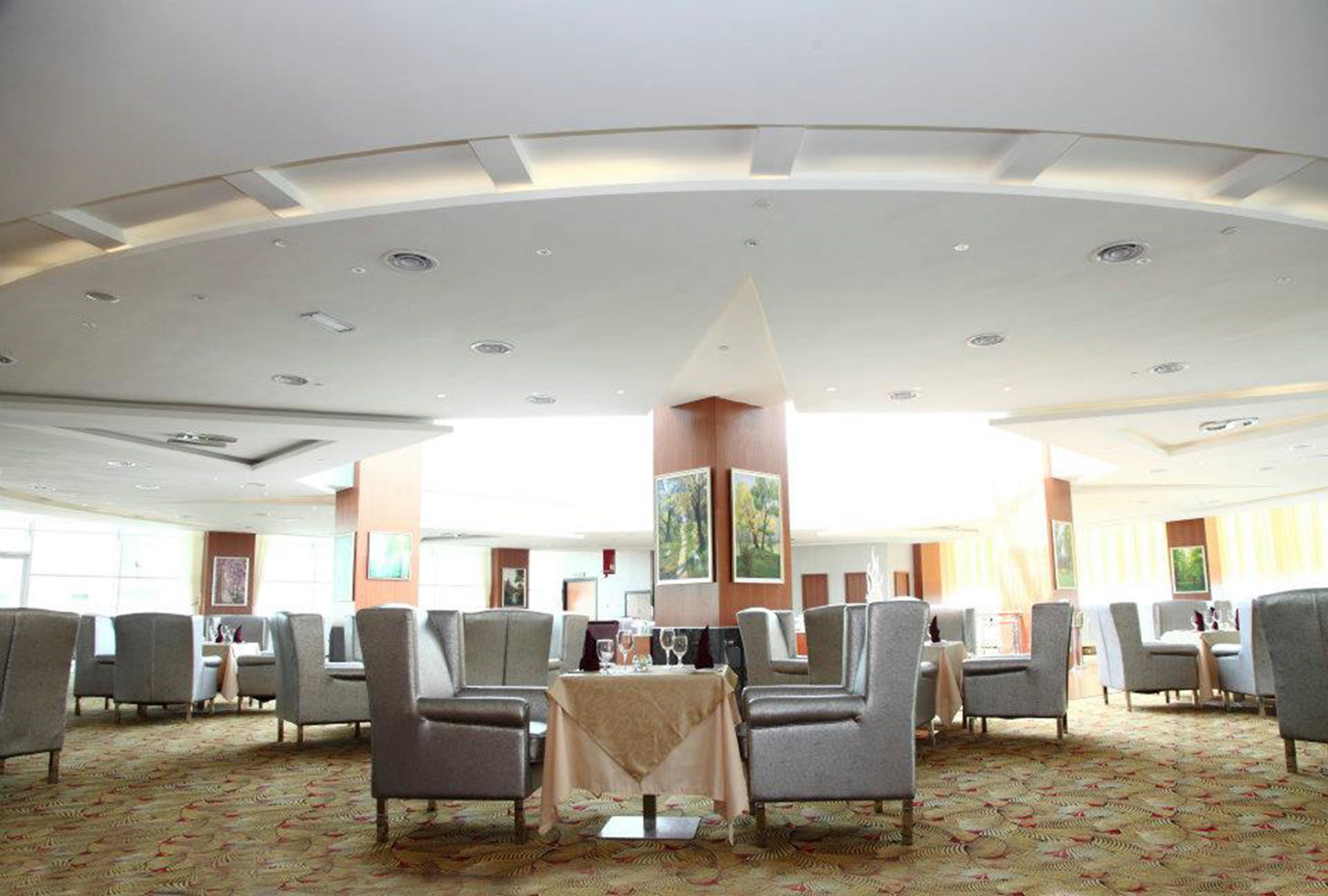 A spacious hotel lobby with a high ceiling, multiple seating areas, and a patterned carpet.