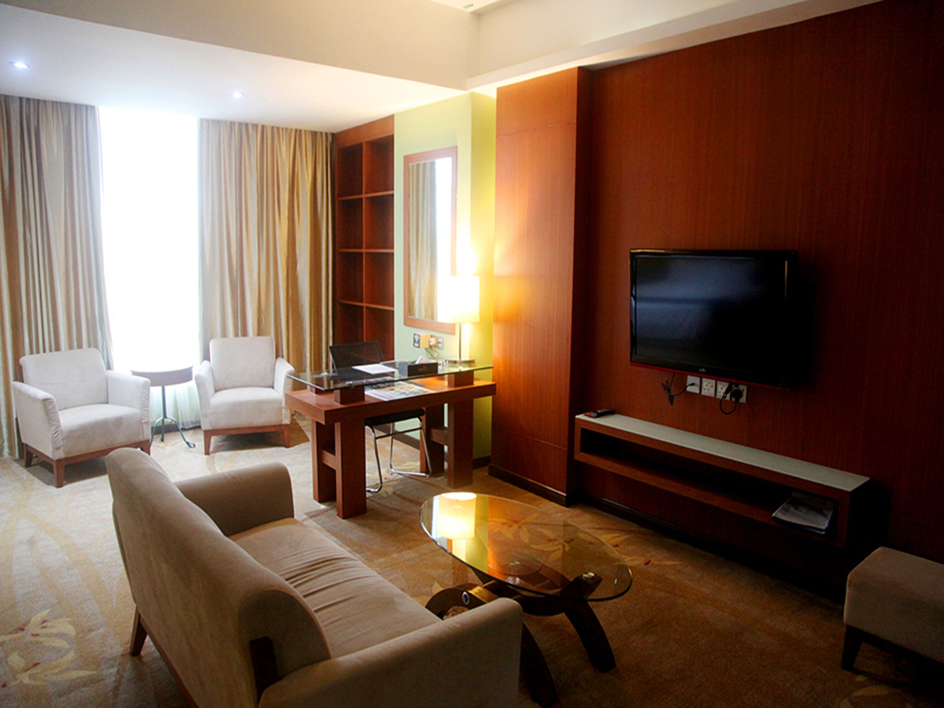Habitación de hotel con sofá, sillones, una mesita de centro, televisor y estantería.