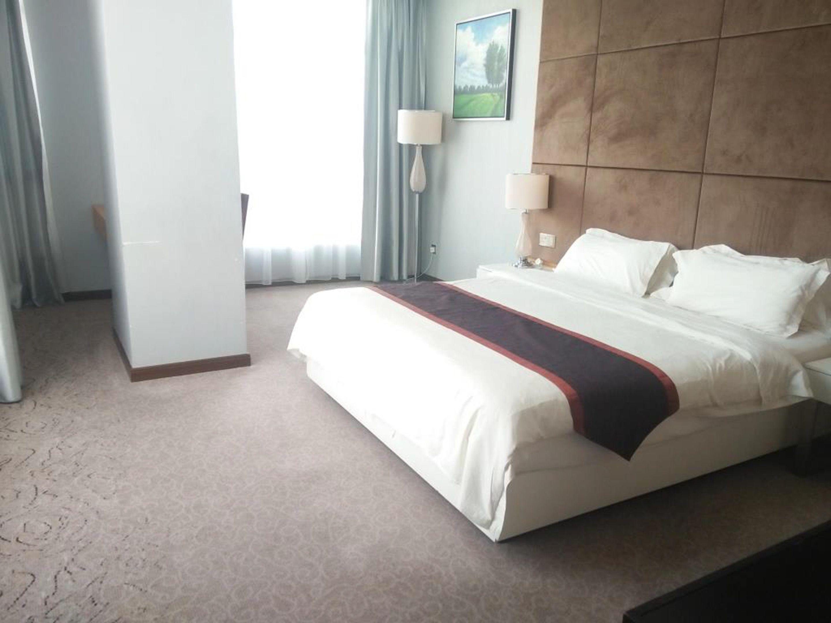 A hotel room with a large bed, a nightstand, a lamp, and a painting on the wall.