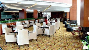 A spacious hotel lobby with multiple dining areas, a central atrium, and a view of the kitchen area.