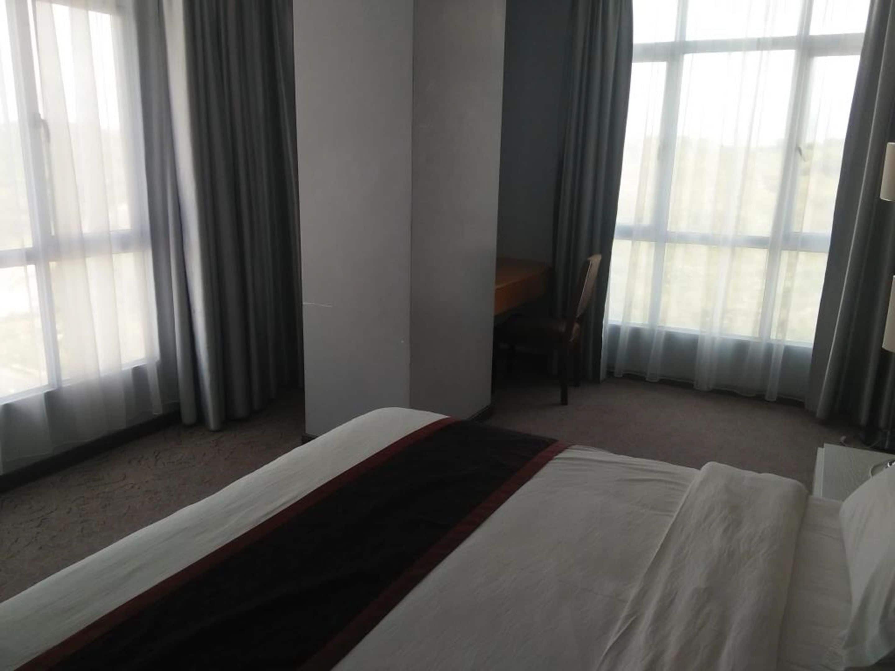Habitación de hotel con cama, escritorio y silla. Amplias ventanas con cortinas.
