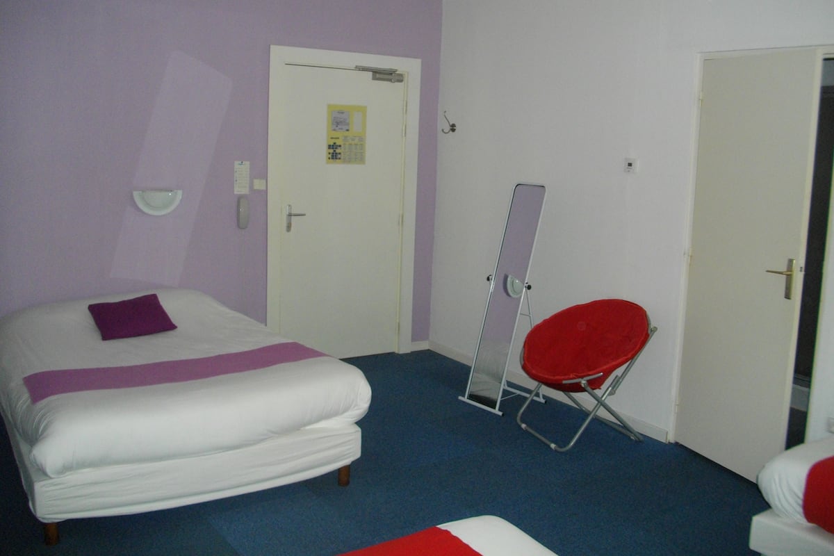 A room with a bed, a red chair, and a door with a mirror.