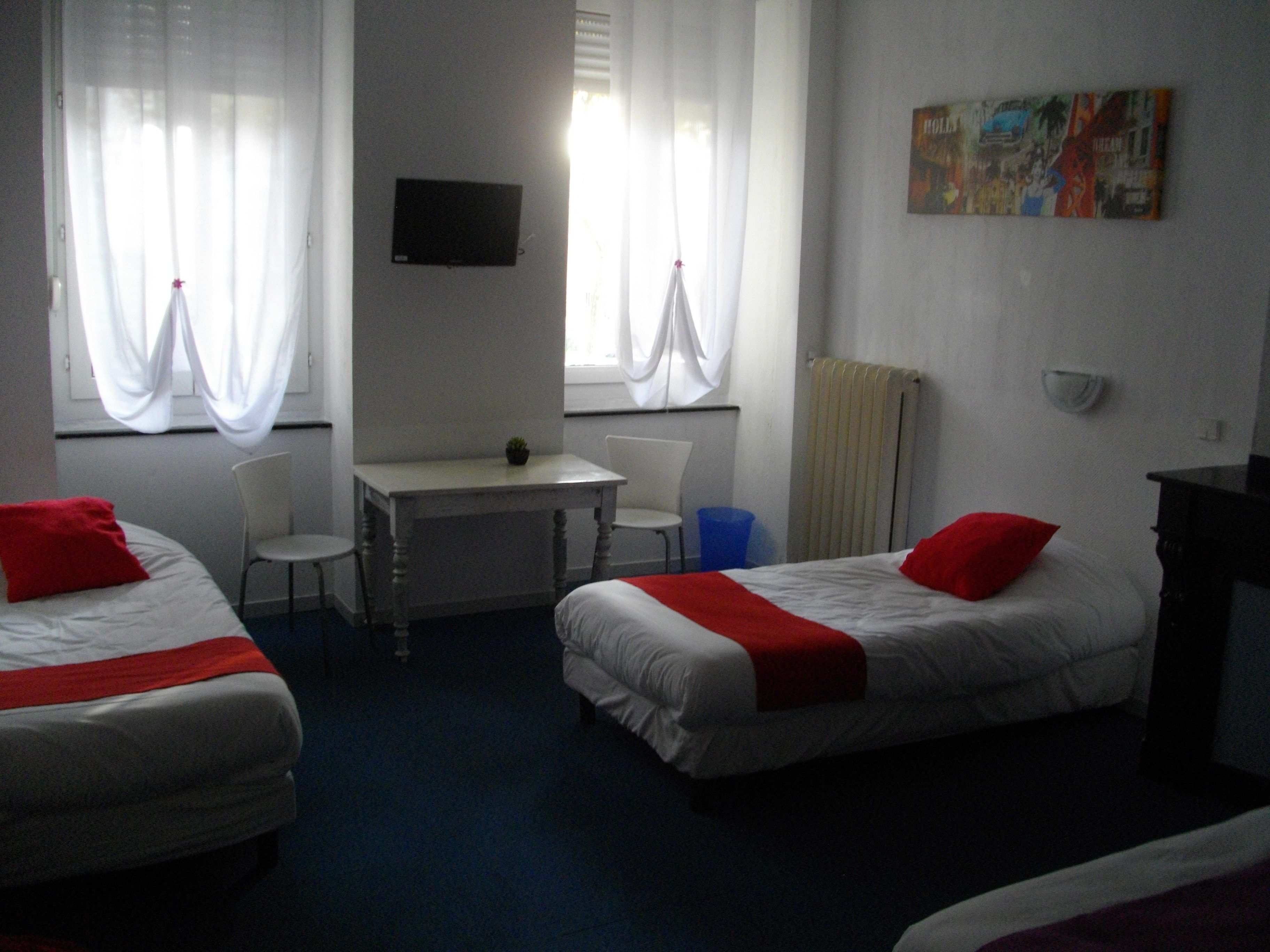 A hotel room with two single beds, a desk, a chair, a TV, and a radiator.