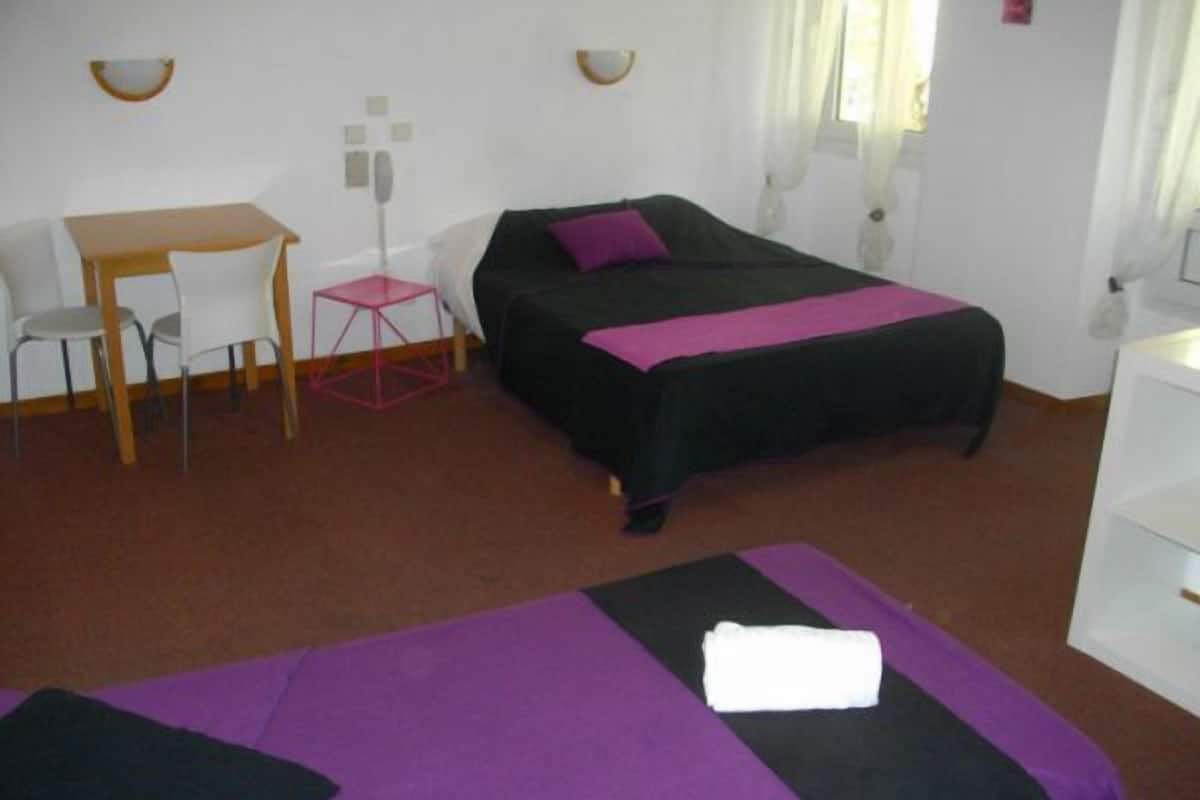 A hotel room with a bed, a desk, a chair, and a small table.