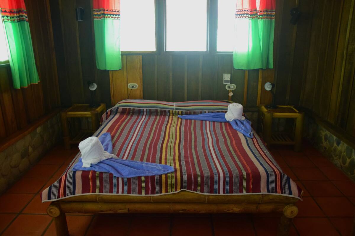 A bed with striped bedding, two pillows, and a white hat on it.