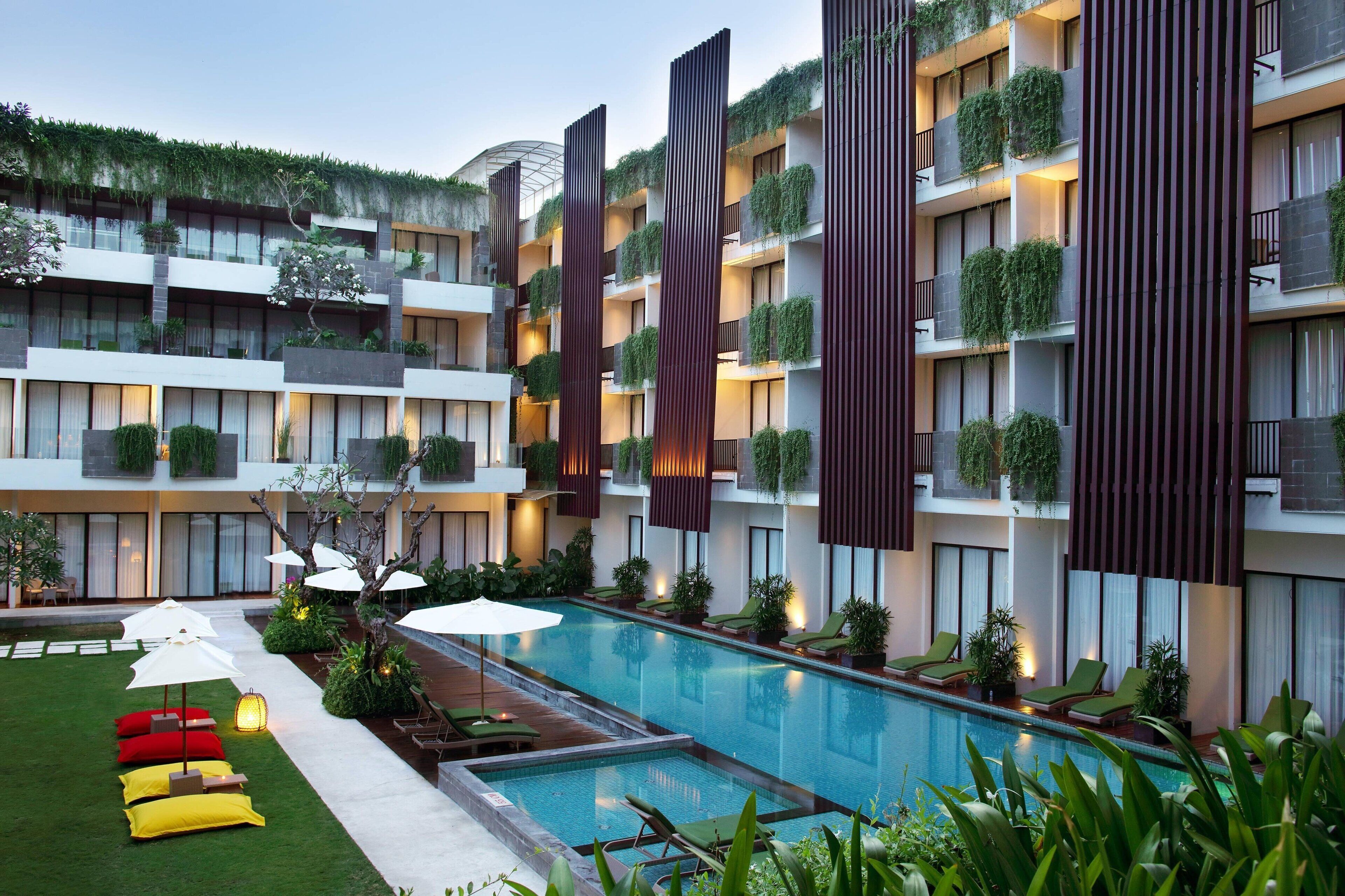 Un hôtel moderne doté d’une piscine, d’un espace extérieur aménagé et de balcons ornés de plantes.