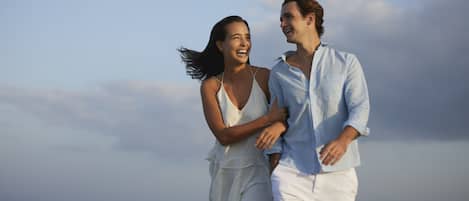 A couple walking on a beach with waves in the background.