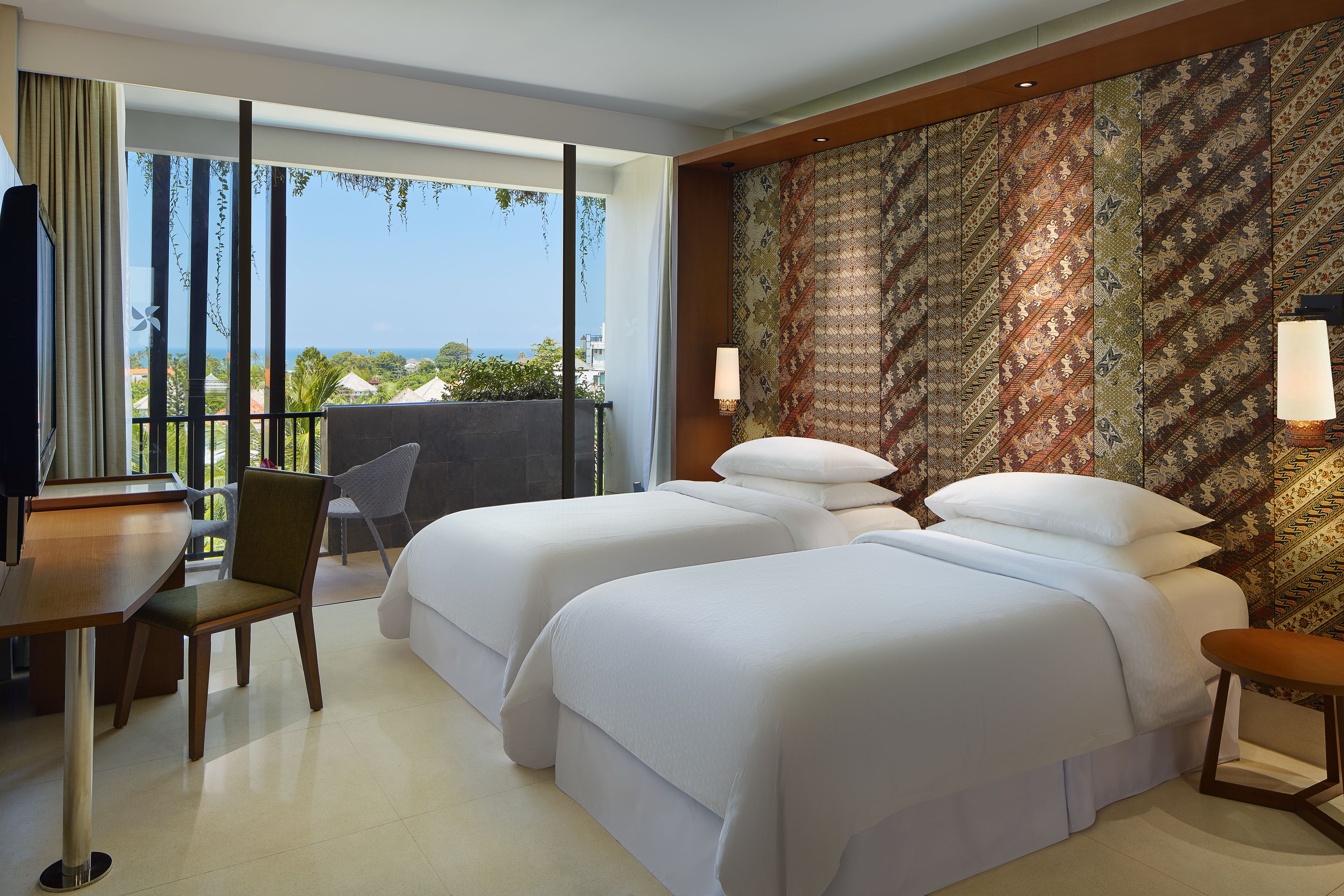 Habitación de hotel con dos camas, un escritorio, una silla y vista al océano.