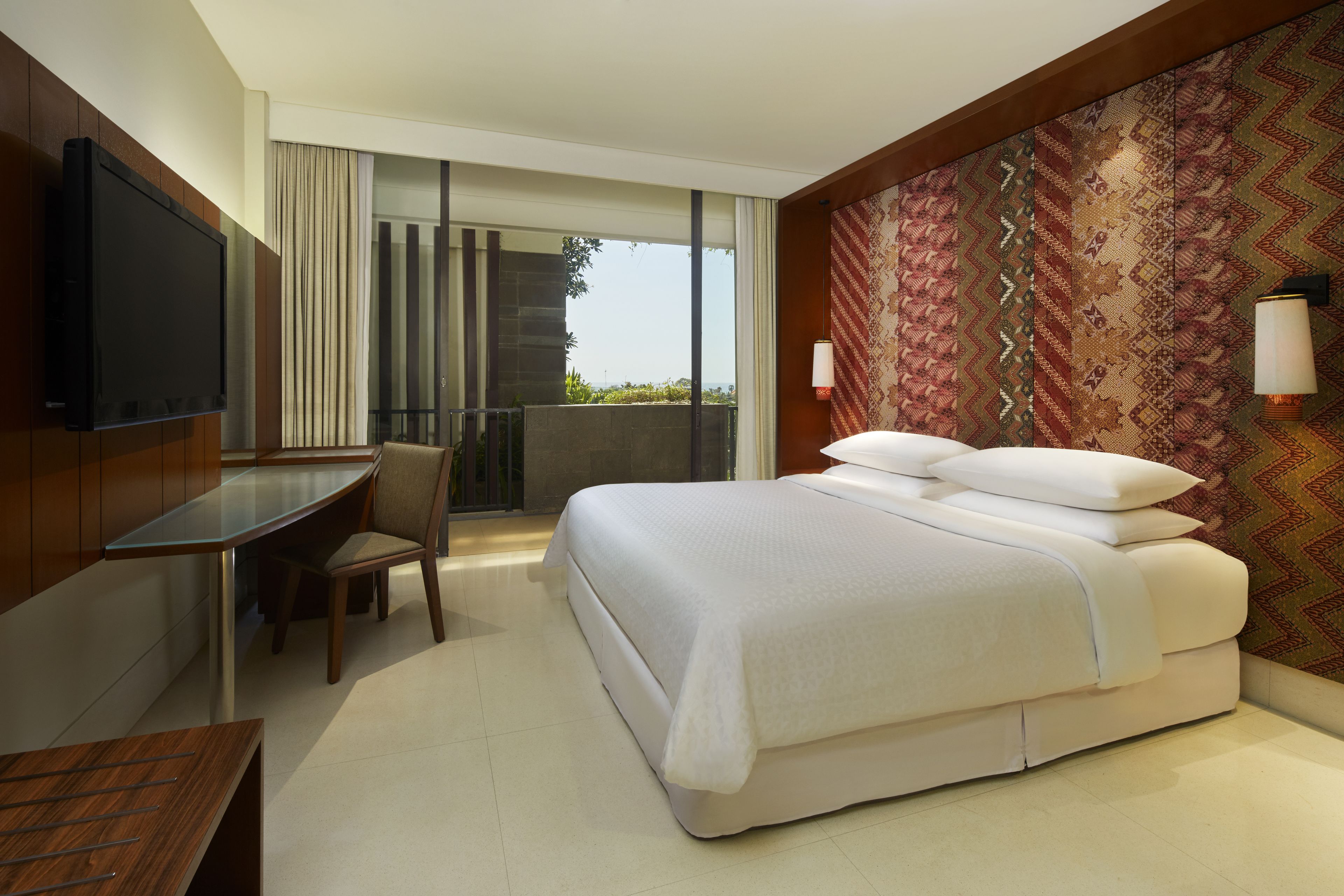 A hotel room with a bed, a desk, a chair, a TV, and a balcony with a view.
