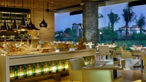 A restaurant with a buffet, tables, chairs, and a view of palm trees and houses. - Four Points by Sheraton Bali Seminyak (Keroboken Kelod)