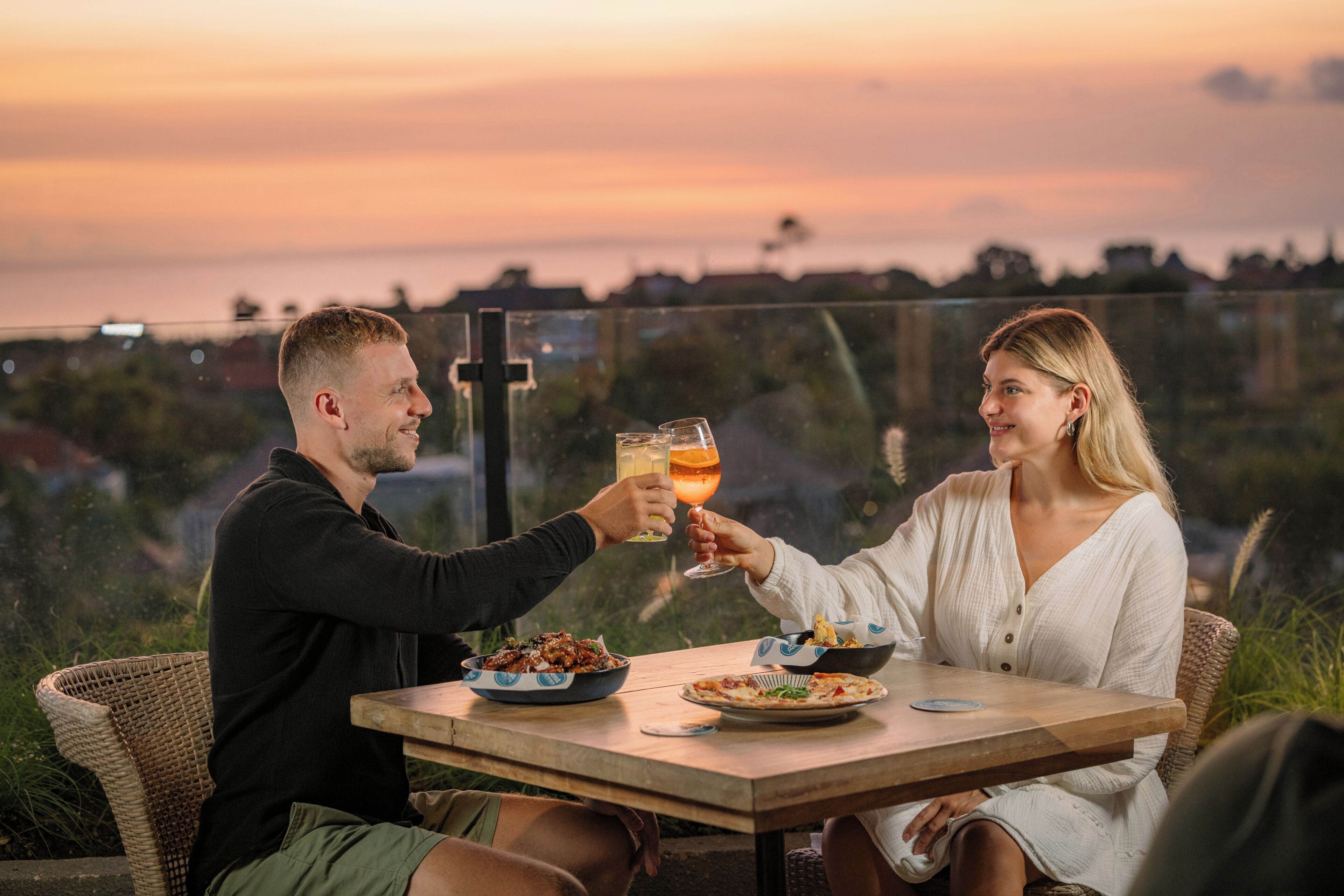 Two people toasting at a table with a sunset view.