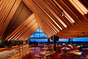 Un restaurante con techo alto y vigas de madera, con mesas y sillas dispuestas para comer.