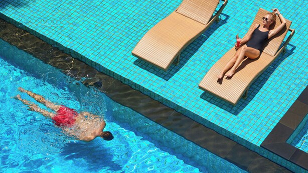A swimming pool with two lounge chairs and a swimmer in the water. - Four Points by Sheraton Bali Seminyak (Keroboken Kelod)