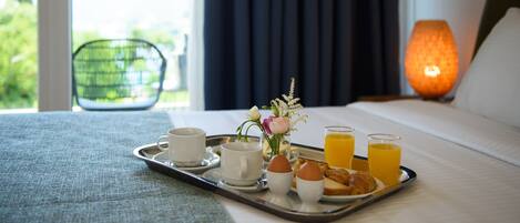 A breakfast tray with eggs, toast, juice, and a vase of flowers on a bed in a hotel room.