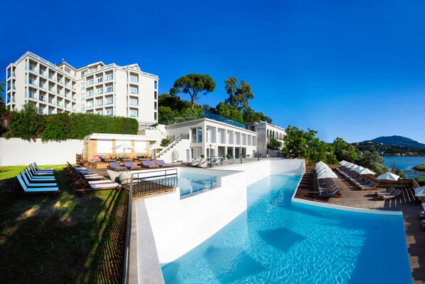 A resort with a large infinity pool, a white building with balconies, and a view of the sea. - The Royal Hotel (Corfu)