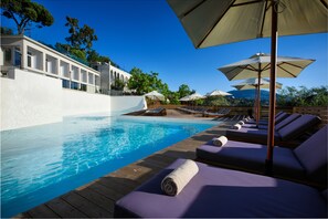 A poolside area with lounge chairs and umbrellas, a wooden deck, and a clear blue pool. - The Royal Hotel (Corfu)