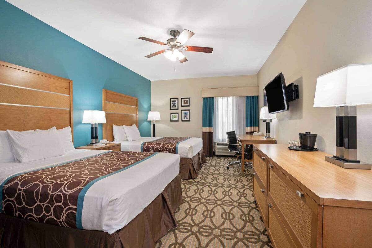 A hotel room with two beds, a desk, a television, and a ceiling fan.