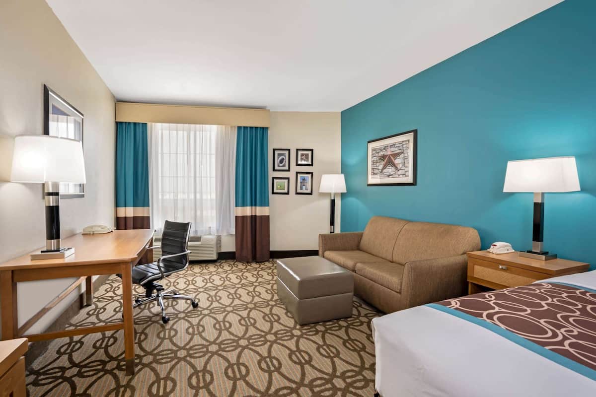 A hotel room with a bed, a desk, a chair, a sofa, a nightstand, and a lamp.
