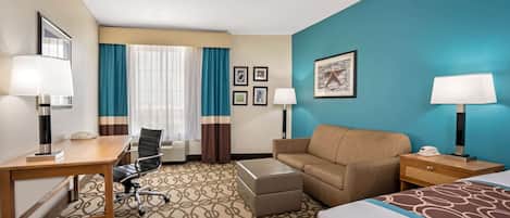 A hotel room with a bed, a desk, a chair, a sofa, a nightstand, and a lamp.