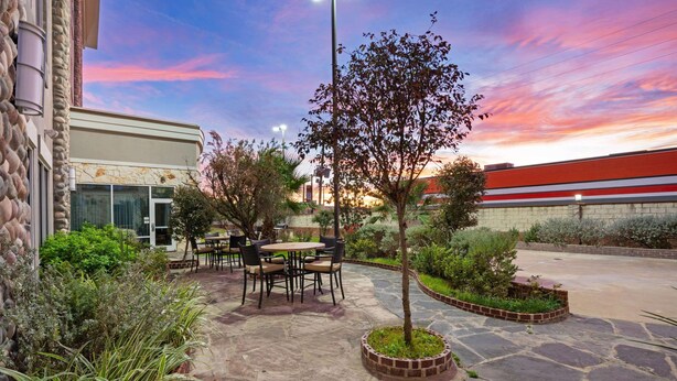 An outdoor patio area with stone flooring, a small tree, and a seating arrangement. - La Quinta by Wyndham Houston Willowbrook Vintage Park (Houston)