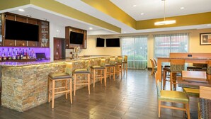 A bar area with a stone counter, multiple bar stools, a television, and a dining table with chairs. - La Quinta by Wyndham Houston Willowbrook Vintage Park (Houston)