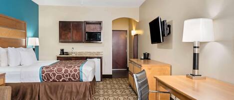 A hotel room with a bed, desk, chair, ceiling fan, TV, microwave, and a small kitchenette.