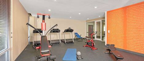 Une salle de sport équipée de tapis de course, d’un rameur, d’un banc et d’un tapis bleu.
