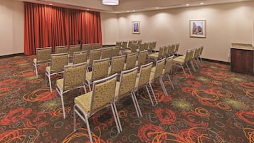 A conference room with rows of chairs, a red curtain, and two framed pictures on the walls.