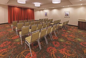 Una sala conferenze con file di sedie, una tenda rossa e due quadri appesi alle pareti.