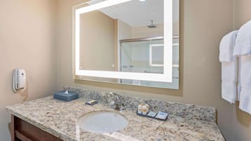 Un baño con encimera de granito, un lavabo, un espejo y un perchero para toallas.