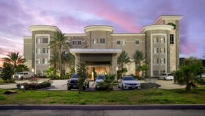 A multi-story hotel with a central entrance, palm trees, and parked cars. - La Quinta by Wyndham Houston Willowbrook Vintage Park (Houston)